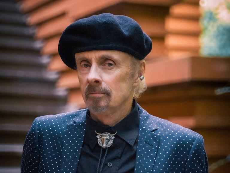 Der Autor T.C. Boyle schaut ernst in die Kamera. Er hat einen kurzen, grau melierten Bart und trägt eine schwarze Baskenmütze, ein schwarzes Hemd und darüber ein blaues Jackett mit weißen Punkten.