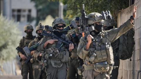 Mehrere israelische Soldaten laufen in voller Montur und schwer bewaffnet durch eine Straße.