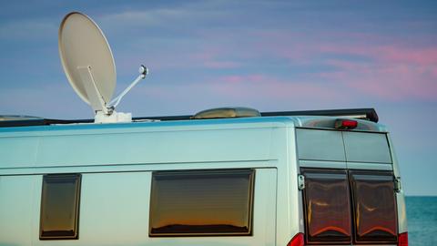 Ein Camper mit Satellitenschüssel auf dem Dach vor einem Sonnenuntergang am Meer.