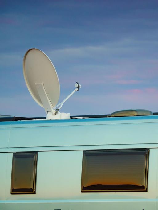 Ein Camper mit Satellitenschüssel auf dem Dach vor einem Sonnenuntergang am Meer.