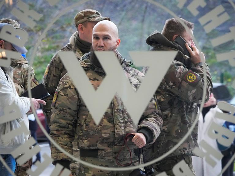 Männer in Camouflage-Anzügen stehen hinter einer Glastür, an der das große "W" der Wagner-Gruppe prangt.