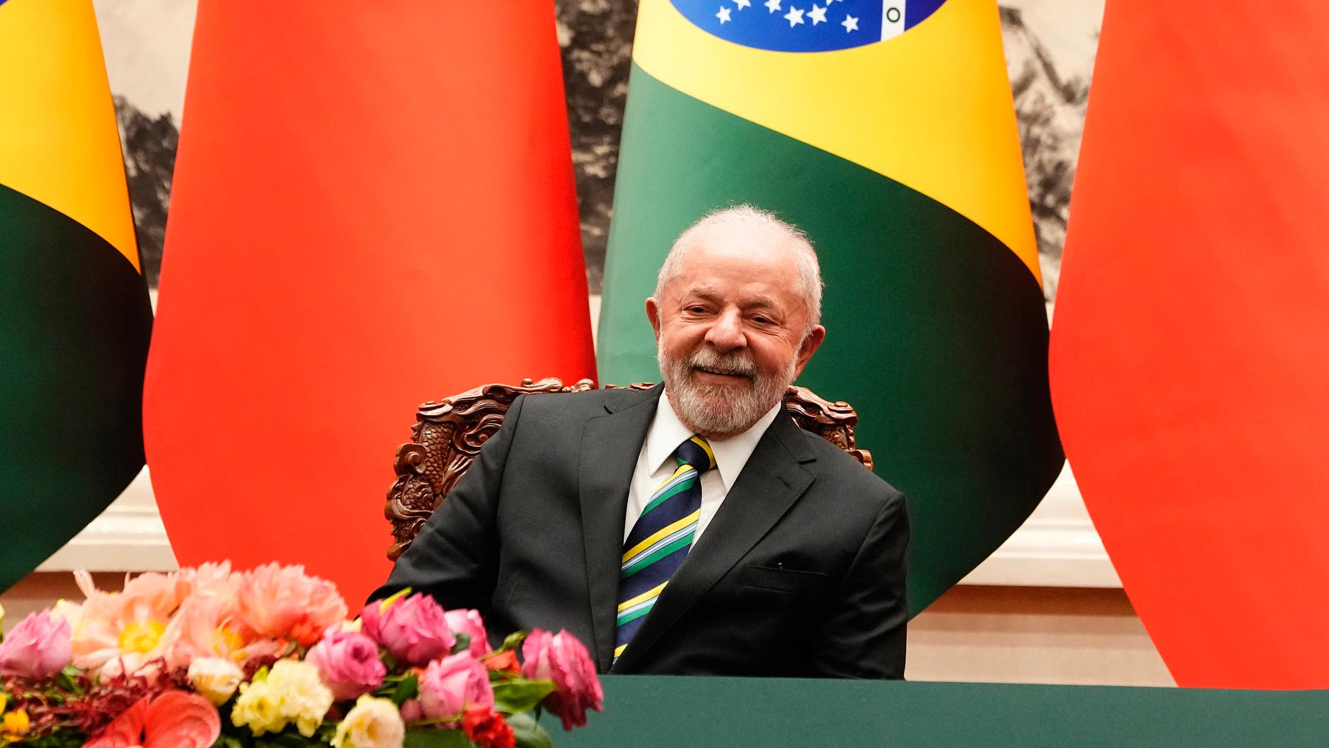 Luiz Inacio Lula da Silva sitzt vor chinesischen und brasilianischen Flaggen und lächelt.