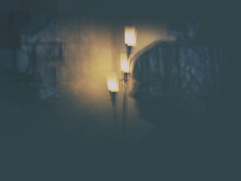 Die Illustration zeigt eine Stehlampe und eine Frau als Spiegelung in einer Glastür nachts