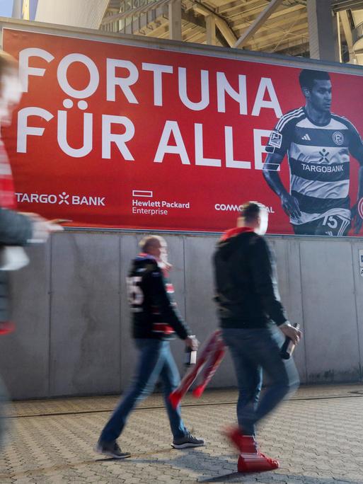 Zuschauer des Spiels Fortuna Düsseldorf gegen Kaiserslautern gehen an einem Transprent vorbei "Fortuna für Alle". Die Tickets für das Spiel sind kostenlos an die Fans abgegeben worden.