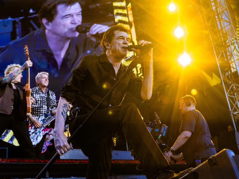 Die Toten Hosen auf der Bühne. Sänger Campino ist vorn und hält sich ein Mikrofon an den Mund. 