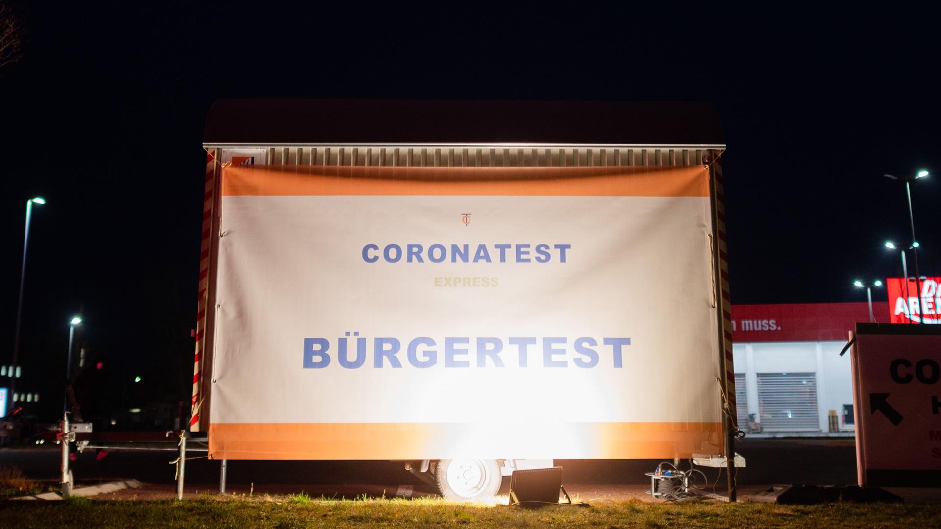 Ein Schild „Coronatest express - Bürgertest“ hängt an einem mobilen Corona-Testzentrum auf einem Parkplatz.