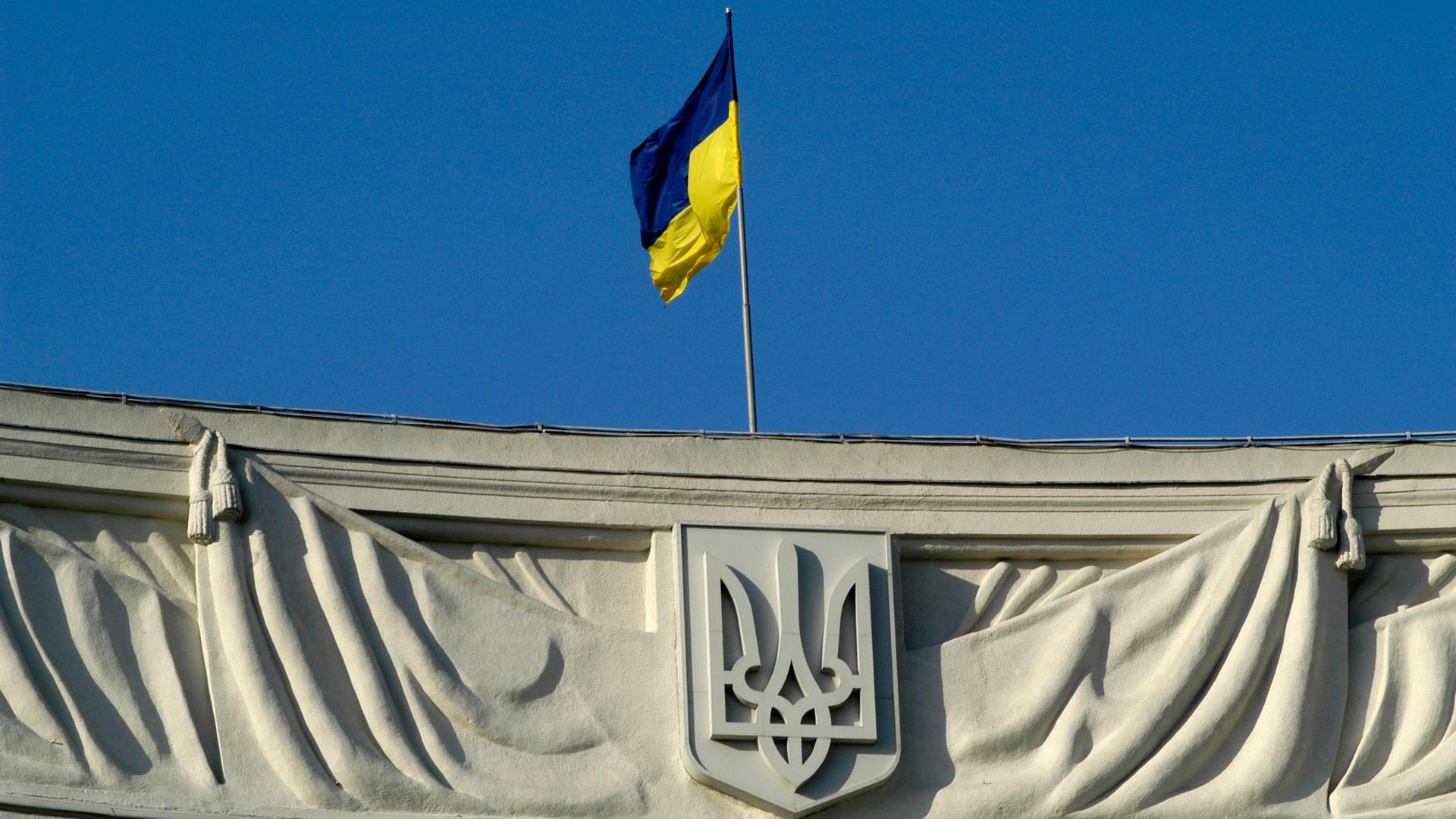 Auf einem Gebäude ist eine ukrainische Flagge und das ukrainische Unabhänigkeitswappen in einer Nahaufnahme zu sehen. 