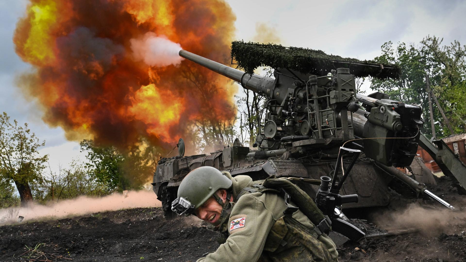 Ein Panzer feuert an der Frontlinie zwischen Ukraine und Russland. Ein Soldat geht in Deckung