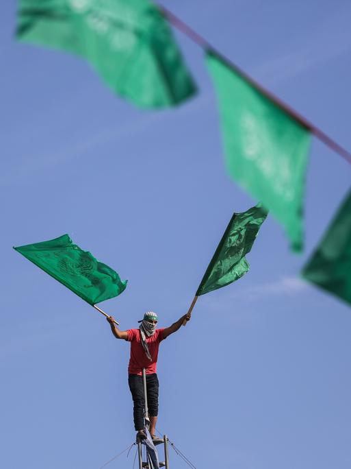 Ein maskierter Hamas-Anhänger schwenkt die Hamas-Flagge. Er nimmt an einer Kundgebung zum 34. Jahrestag der Gründung der islamistischen Bewegung Hamas im Flüchtlingslager Jabalya im nördlichen Gazastreifen teil.
