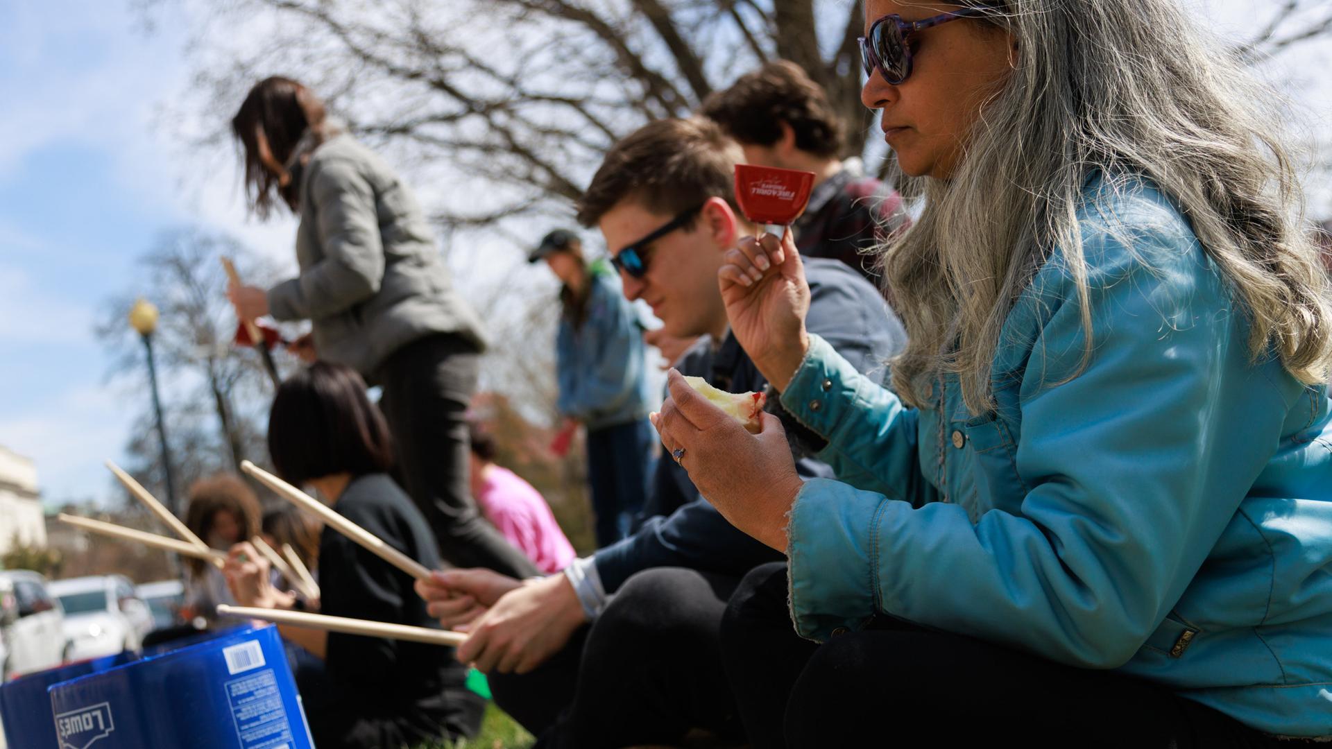 Klimaaktivisten sitzen bei einer Protestaktion auf dem Boden und trommeln auf Eimern.