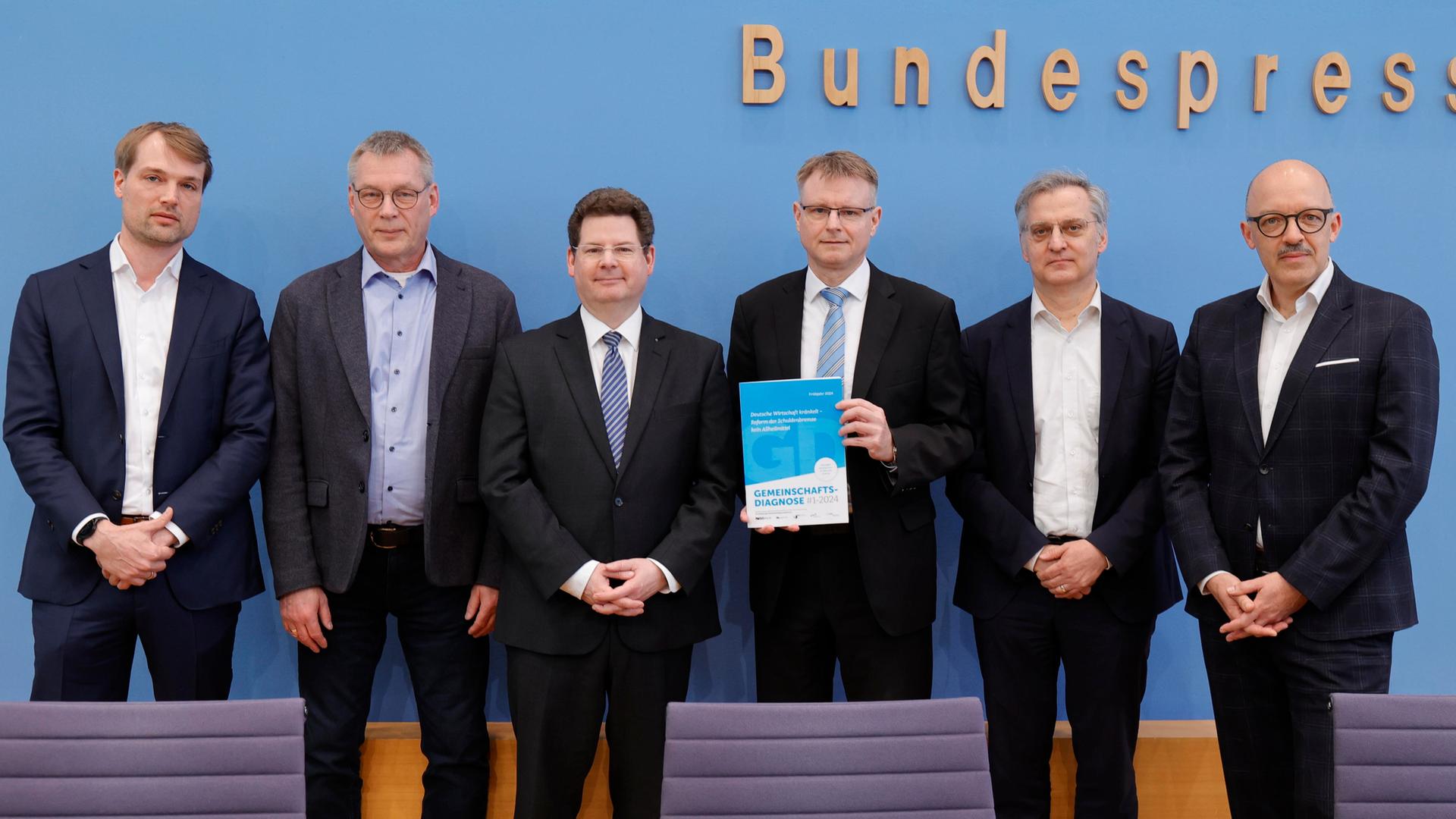 Von links nach rechts stehen die Wirtschaftsforscher Timm Bönke, Klaus-Jürgen Gern, Oliver Holtemöller, Stefan Kooths, Torsten Schmidt sowie Timo Wollmershäuser und präsentieren ihre Gemeinschaftsdiagnose.