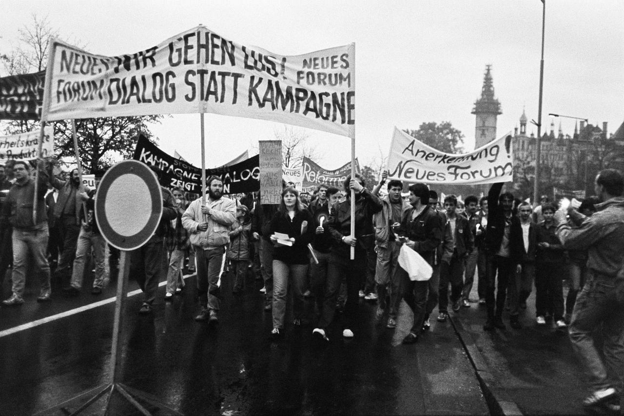 Schwarzweißbild einer Montagsdemonstration in Schwerin im Oktober 1989, kurz vor dem Mauerfall. Die Demonstranten fordern auf den Transparenten u.a. die Anerkenneung des "Neuen Forum".