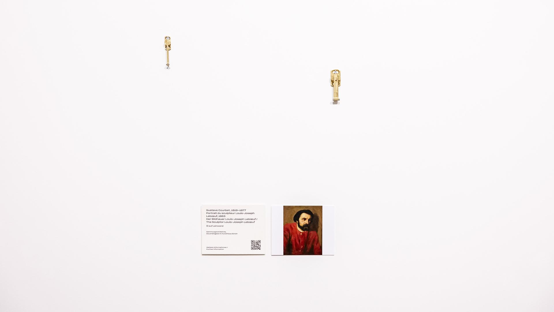 Eine leere Wand mit Aufäengungsvorrichtungen und einer kleinen Informationstafel am Platz wo das Bild "Portrait du Sculpteur Louis-Joseph" von Gustave Courbet abgehaengt wurde