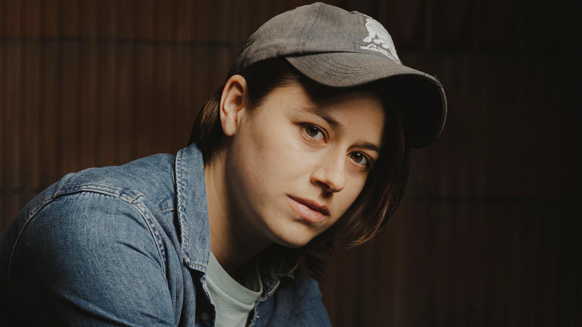 Die Schweizer Autorin Sarah Elena Müller. Sie posiert mit Basecap und in Jeanshemd und weißem T-Shirt vor der Kamera.