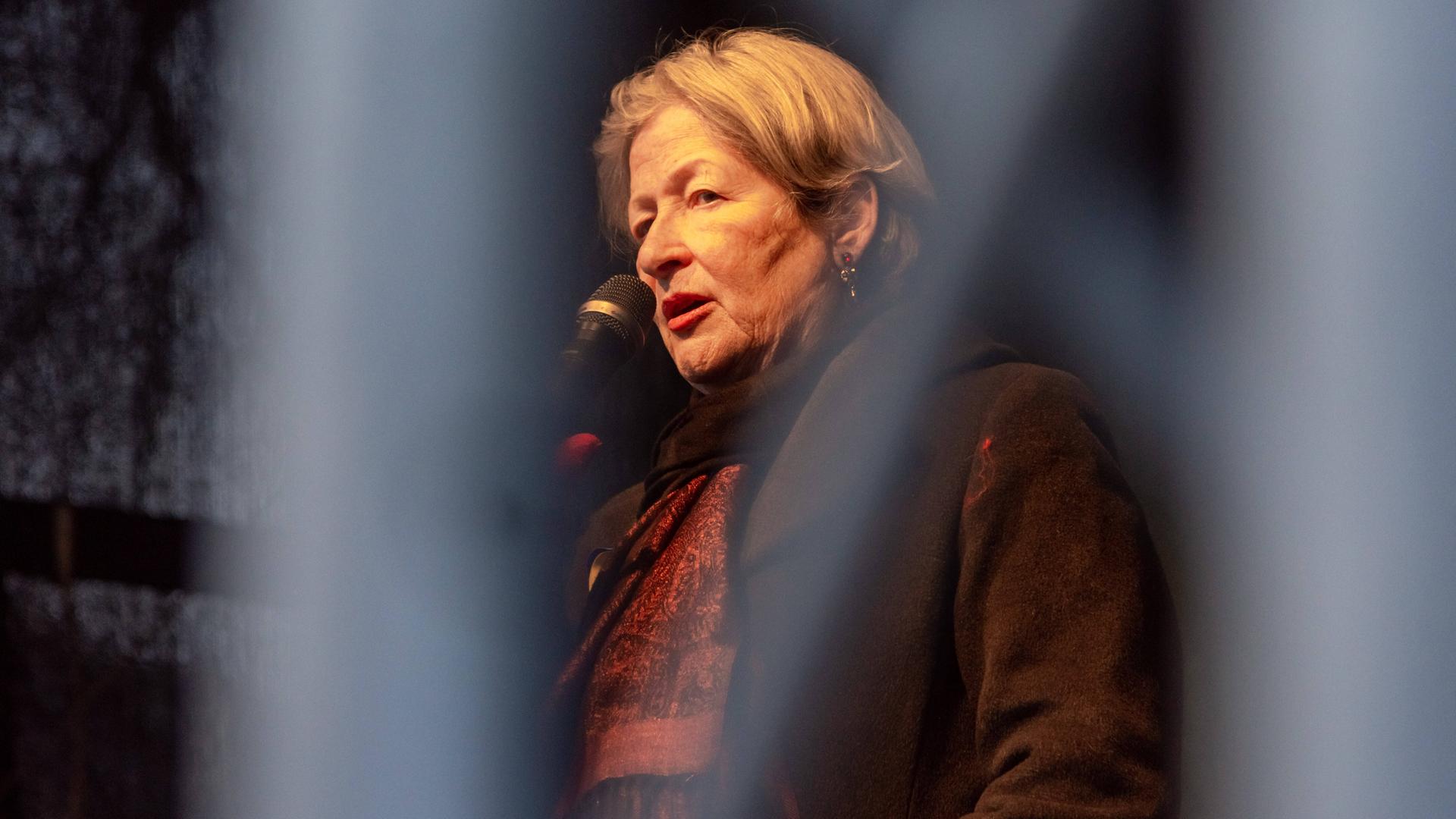 Die österreichische Schriftstellerin Susanne Scholl spricht bei einer Demonstration auf einer Bühne in ein Mikrofon 