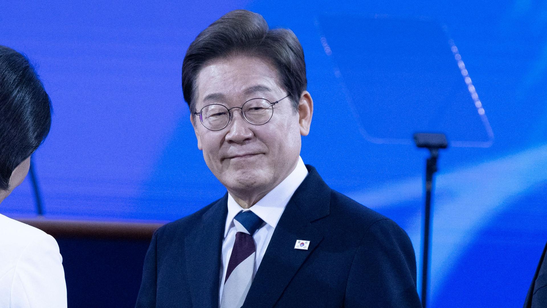 Südkoreas Präsident Lee lächelt in die Kamera. Neben ihm steht eine Frau mit dem Rücken zum Betrachter.