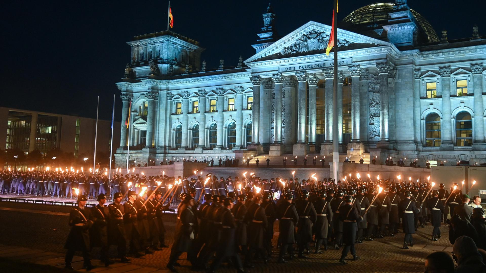 Soldaten stehen in der Nacht mit Fackeln in Formation vorm illuminierten und beflaggten Reichstagsgebäude in Berlin.