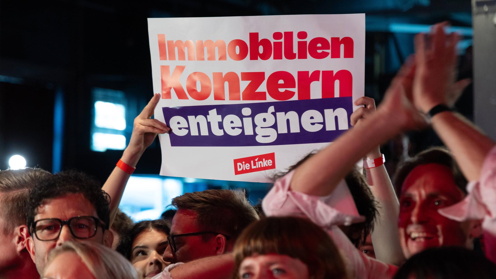 Das Bild zeigt ein Plakat. Darauf steht: "Immobilienkonzern enteignen." Das Plakat wird aus einer Menschenmenge hochgehalten.