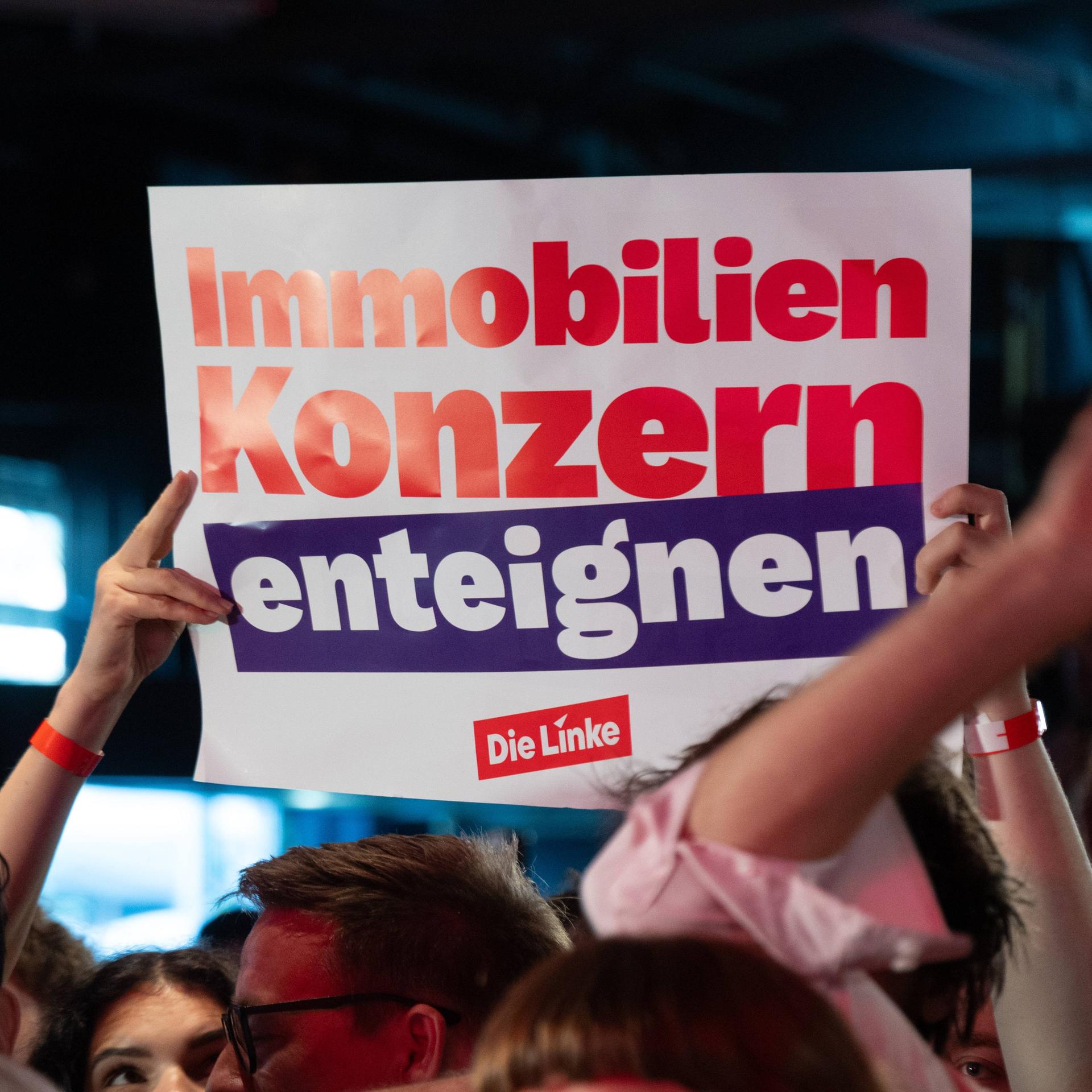 Das Bild zeigt ein Plakat. Darauf steht: "Immobilienkonzern enteignen." Das Plakat wird aus einer Menschenmenge hochgehalten.