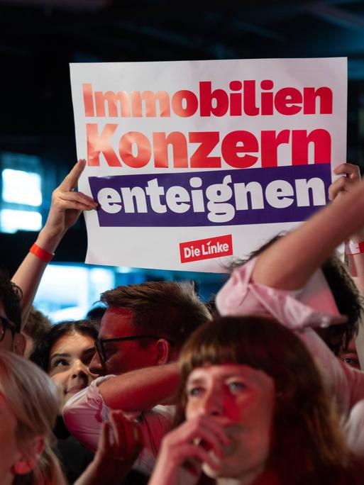 Das Bild zeigt ein Plakat. Darauf steht: "Immobilienkonzern enteignen." Das Plakat wird aus einer Menschenmenge hochgehalten.