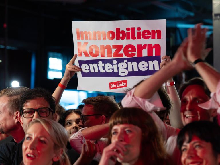 Das Bild zeigt ein Plakat. Darauf steht: "Immobilienkonzern enteignen." Das Plakat wird aus einer Menschenmenge hochgehalten.