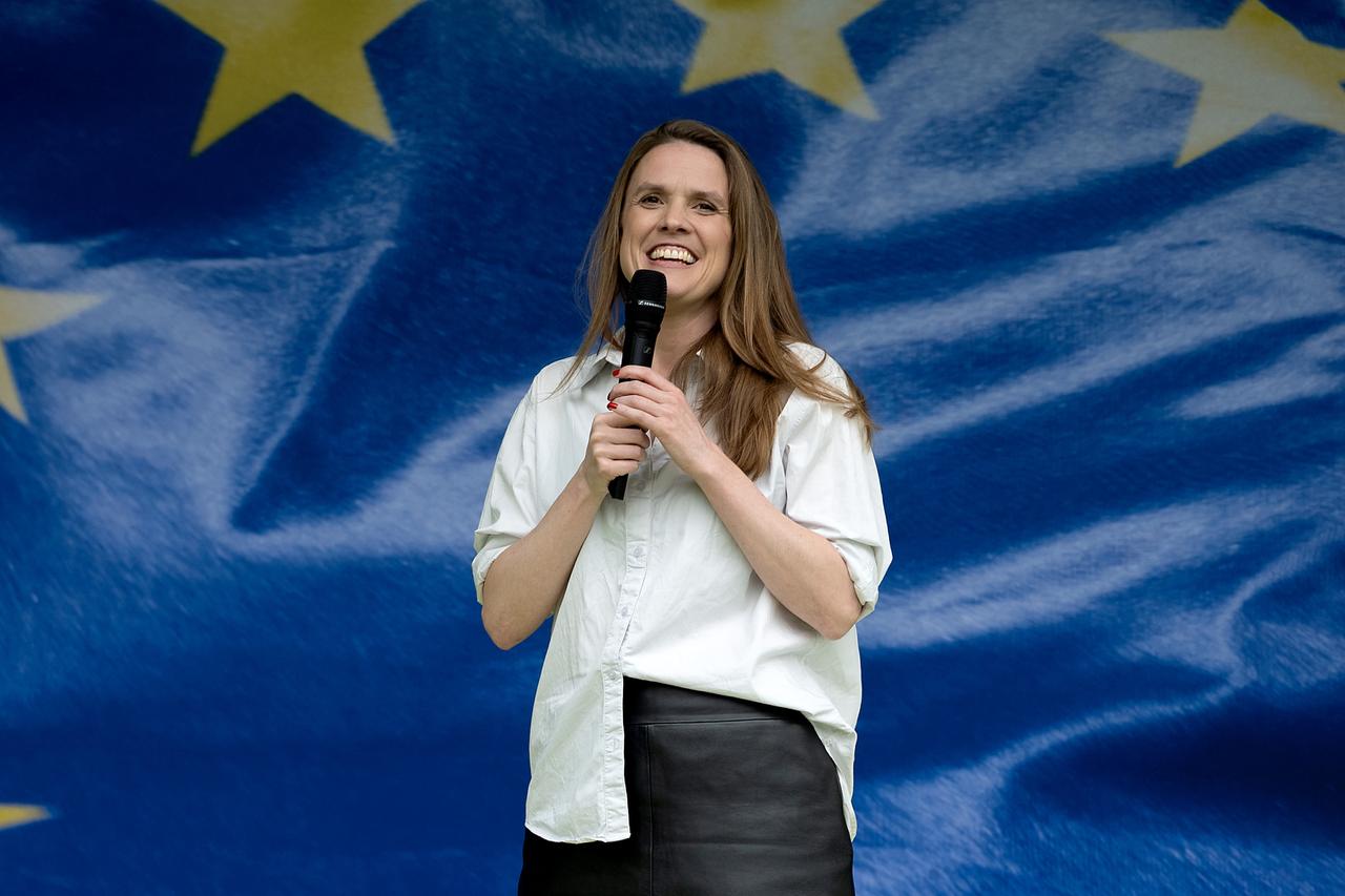 Terry Reintke steht auf einer Bühne. Sie hält ein Mikrofon in den Händen und lächelt. Hinter ihr ein Teil von der Europa-Flagge.