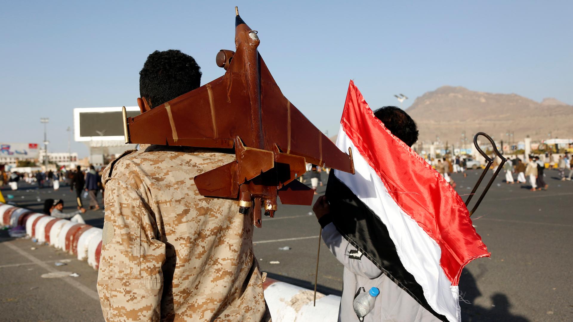 Ein Mann, der die jemenitische Nationalflagge hält, und ein anderer, der eine Düsenflugzeugattrappe trägt, nehmen am 12. Januar 2024 in Sana'a, Jemen, an einer Demonstration gegen die Verletzung der Souveränität des Jemen durch Luftangriffe von US-amerikanischen und britischen Düsenflugzeugen auf Orte in der Hauptstadt Sana'a und einigen Provinzen teil. 