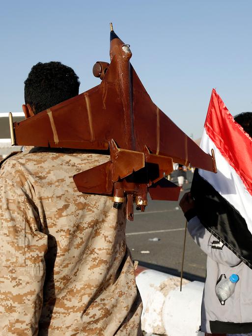 Ein Mann, der die jemenitische Nationalflagge hält, und ein anderer, der eine Düsenflugzeugattrappe trägt, nehmen am 12. Januar 2024 in Sana'a, Jemen, an einer Demonstration gegen die Verletzung der Souveränität des Jemen durch Luftangriffe von US-amerikanischen und britischen Düsenflugzeugen auf Orte in der Hauptstadt Sana'a und einigen Provinzen teil. 