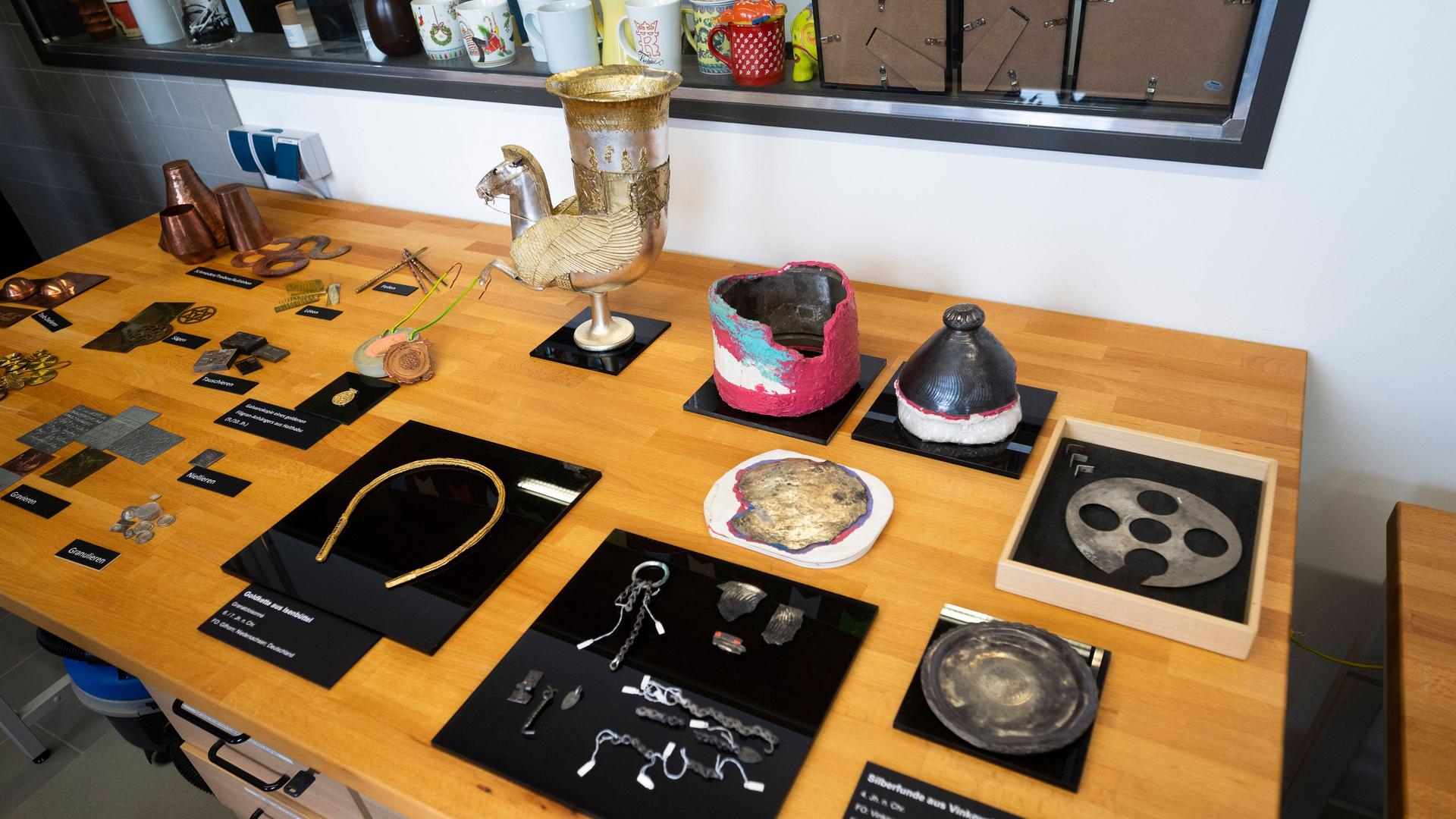 Verschiedene kunsthandwerkliche Gegenstände und Werkzeug zur Restaurierung liegen auf einem Tisch in einer Werkstatt.