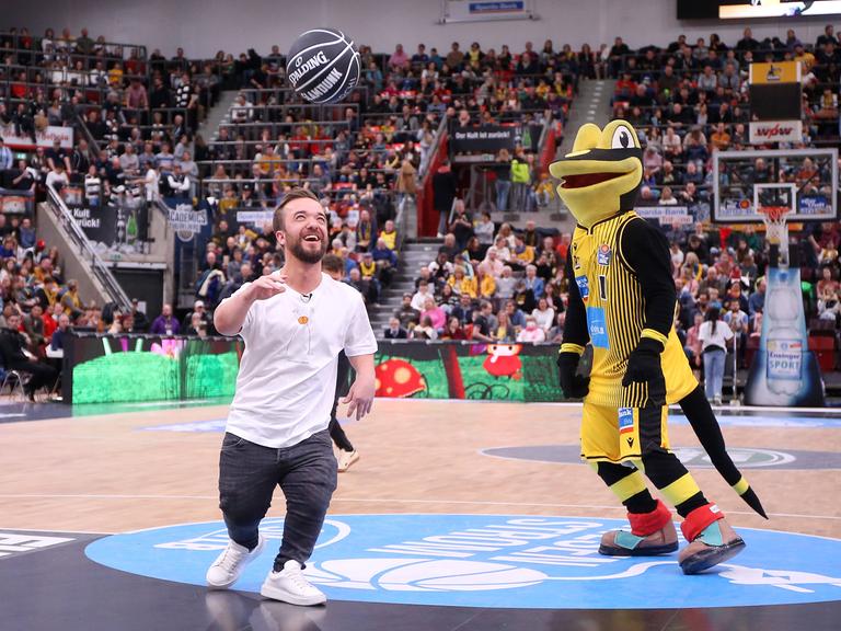 Matthias Mester spielt mit dem Maskottchen Lurchi in Ludwigsburg in einer Halle Basketball.