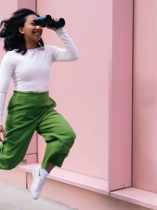 Eine Frau schaut durch ein Fernglas und bewegt sich dabei nach vorne. Es wirkt, als würde sie fliegen. Eine Frau schaut durch ein Fernglas und bewegt sich dabei nach vorne. Es wirkt, als würde sie fliegen.