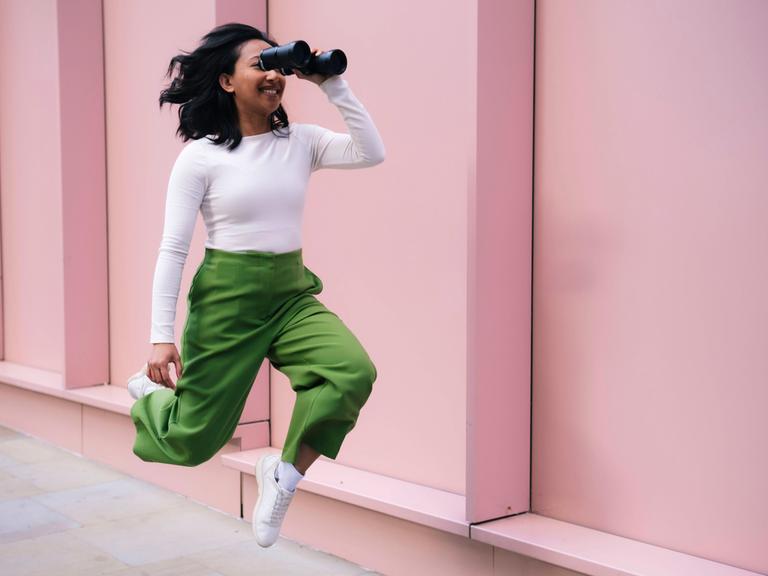 Eine Frau schaut durch ein Fernglas und bewegt sich dabei nach vorne. Es wirkt, als würde sie fliegen. Eine Frau schaut durch ein Fernglas und bewegt sich dabei nach vorne. Es wirkt, als würde sie fliegen.