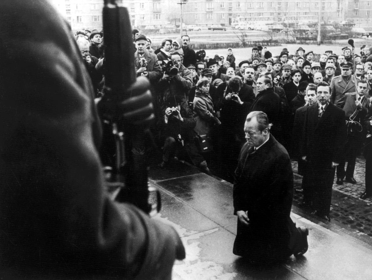 Auf dem Schwarz-Weiß-Bild sieht man den damaligen Bundeskanzler Willy Brandt, wie er vor dem Mahnmal für die Gefallenen des Ghetto-Aufstands in Warschau kniet. Im Hintergrund siehmt man mehrere Journalisten, Fotografen und Zuschauende. Auf dem Schwarz-Weiß-Bild sieht man den damaligen Bundeskanzler Willy Brandt, wie er vor dem Mahnmal für die Gefallenen des Ghetto-Aufstands in Warschau kniet. Im Hintergrund siehmt man mehrere Journalisten, Fotografen und Zuschauende.