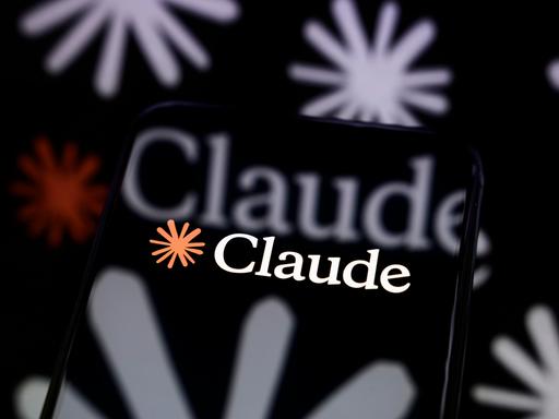 Das Claude-Logo ist auf dem Bildschirm eines Smartphones zu sehen, das auf einer reflektierenden Fläche steht Das Claude-Logo ist auf dem Bildschirm eines Smartphones zu sehen, das auf einer reflektierenden Fläche steht