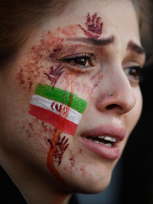 Eine junge Frau mit der von Tränen verschmierten iranischen Flagge und roten Händen auf ihrem Gesicht. Auf einer Demonstration wegen des Todes von Mahsa Amini im Iran. Paris, 9.Oktober 2022. 