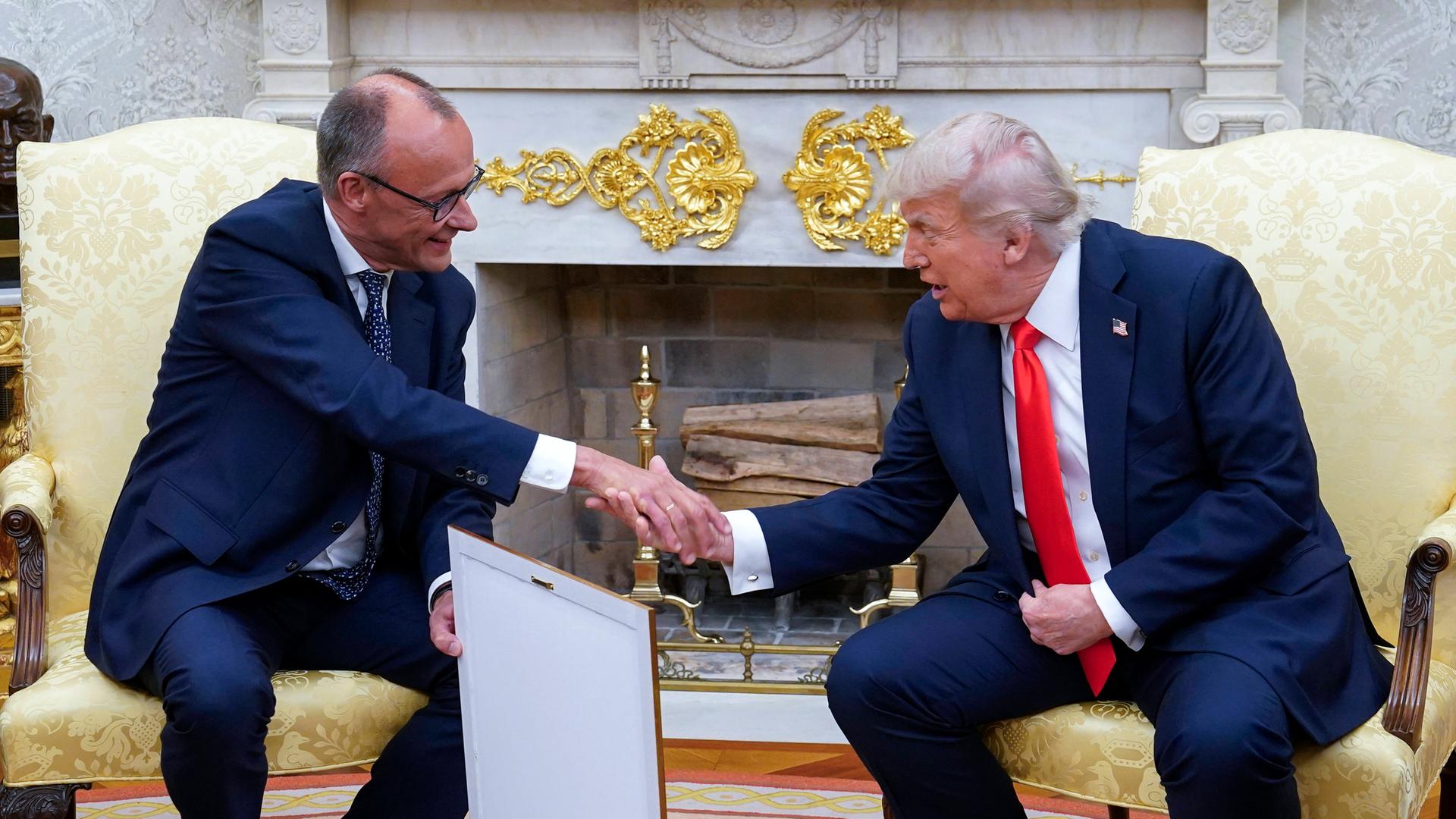 Bundeskanzler Friedrich Merz schüttelt im Oval Office die Hand von US-Präsident Donald Trump. In der anderen Hand hält Merz sein Gastgeschenk: ein gerahmtes Abbild der Geburtsurkunde von Trumps Großvater.