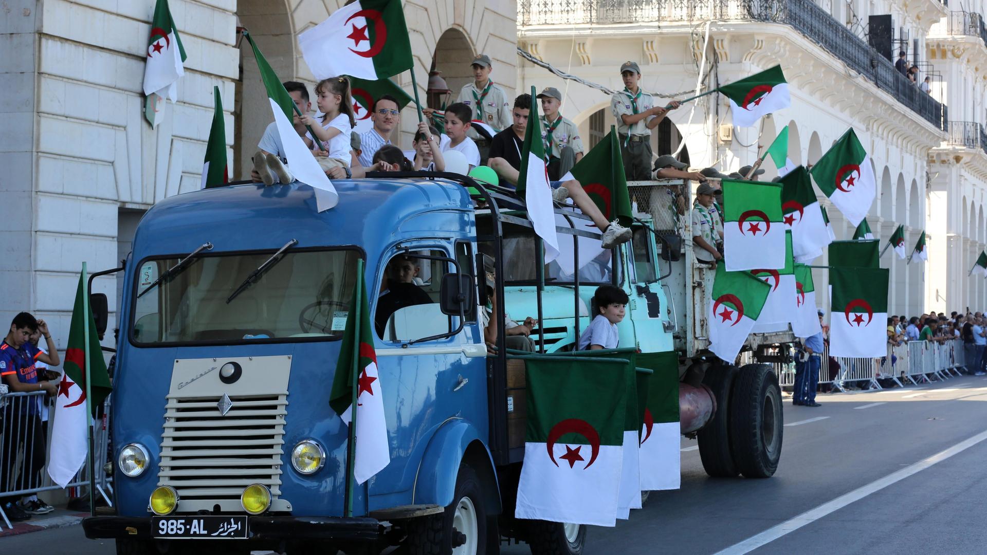 Kinder und Jugendliche auf einem Lkw schwenken algerische Fahnen bei einem Umzug in Algeriens Hauptstadt Algier.