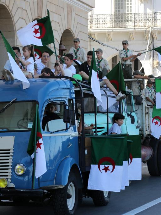 Kinder und Jugendliche auf einem Lkw schwenken algerische Fahnen bei einem Umzug in Algeriens Hauptstadt Algier.