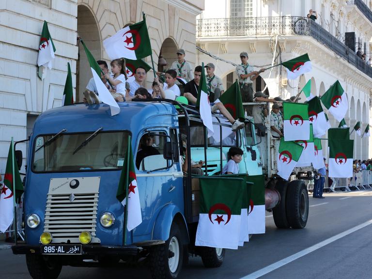 Kinder und Jugendliche auf einem Lkw schwenken algerische Fahnen bei einem Umzug in Algeriens Hauptstadt Algier.