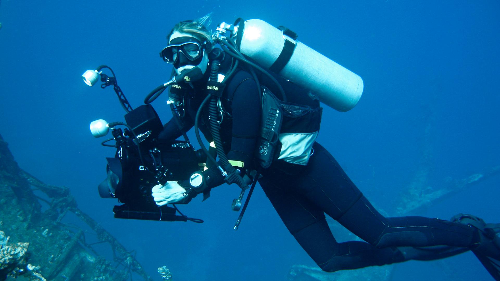 Die Dokumentarfilmerin Christina Karliczek bei der Arbeit, in Taucherausrüstung und Kamera unter Wasser. 
