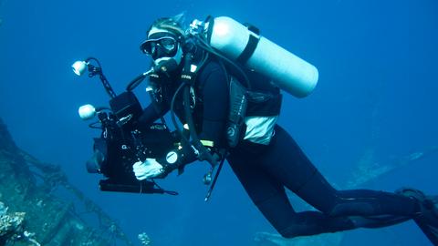 Die Dokumentarfilmerin Christina Karliczek bei der Arbeit, in Taucherausrüstung und Kamera unter Wasser. 
