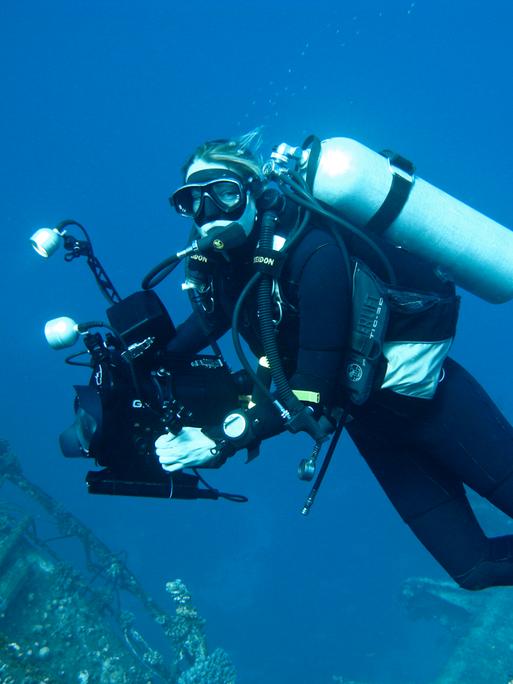 Die Dokumentarfilmerin Christina Karliczek bei der Arbeit, in Taucherausrüstung und Kamera unter Wasser. 
