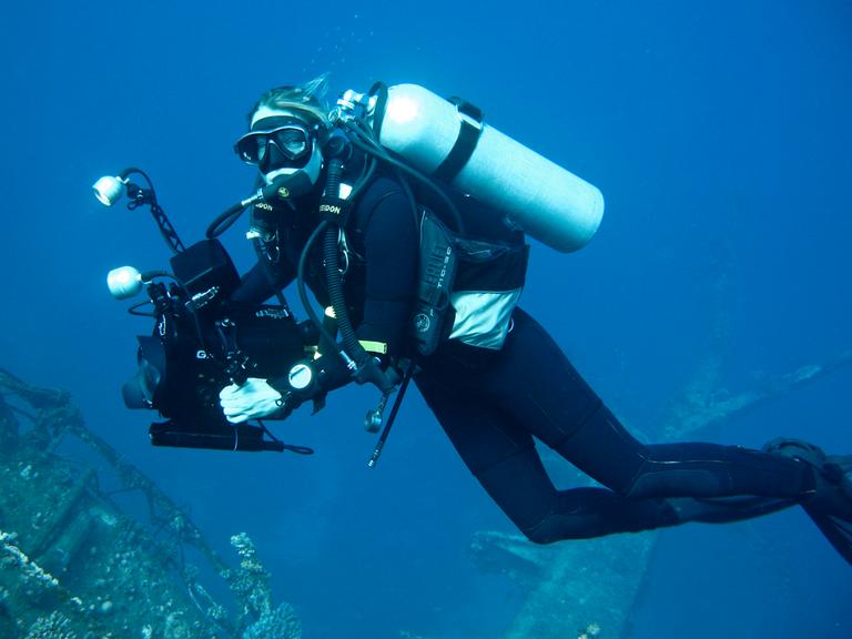 Die Dokumentarfilmerin Christina Karliczek bei der Arbeit, in Taucherausrüstung und Kamera unter Wasser. 
