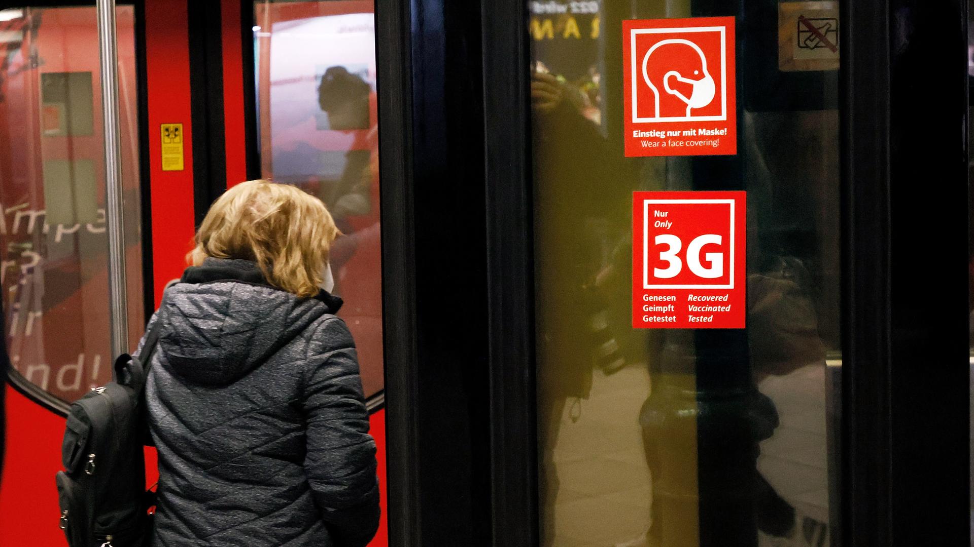 ﻿﻿Ein Fahrgast betritt eine Bahn, an der Schilder mit dem Hinweis auf die Maskenpflicht und und die 3G-Regel zu sehen sind. 