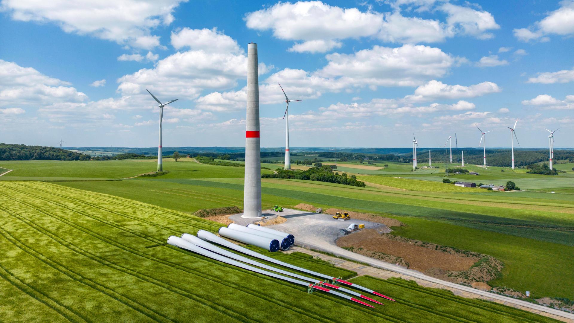 In einem Windpark werden neue Windenergieanlage gebaut. Turmelemente und Rotoren liegen zur Montage bereit.