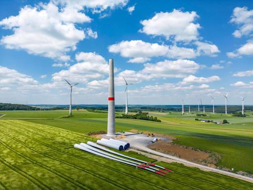 In einem Windpark werden neue Windenergieanlage gebaut, Turmelemente und Rotoren liegen zur Montage bereit.