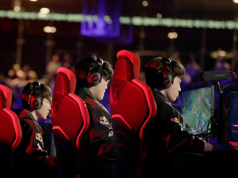 Spieler der koreanischen Mannschaft T1 spielen bei einem E-Sport-Showevent. Sie sitzen in roten Sitzen vor Bildschirmen.