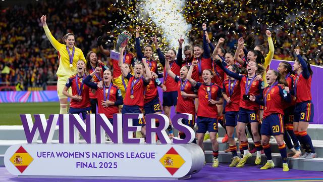 Zu sehen ist das spanische Frauen-Fußball-Nationalteam beim Jubel auf einem Podest. Die Spielerinnen recken ihre Hände hoch und halten den Pokal. Im Hintergund wird Konfetti in die Luft geblasen.