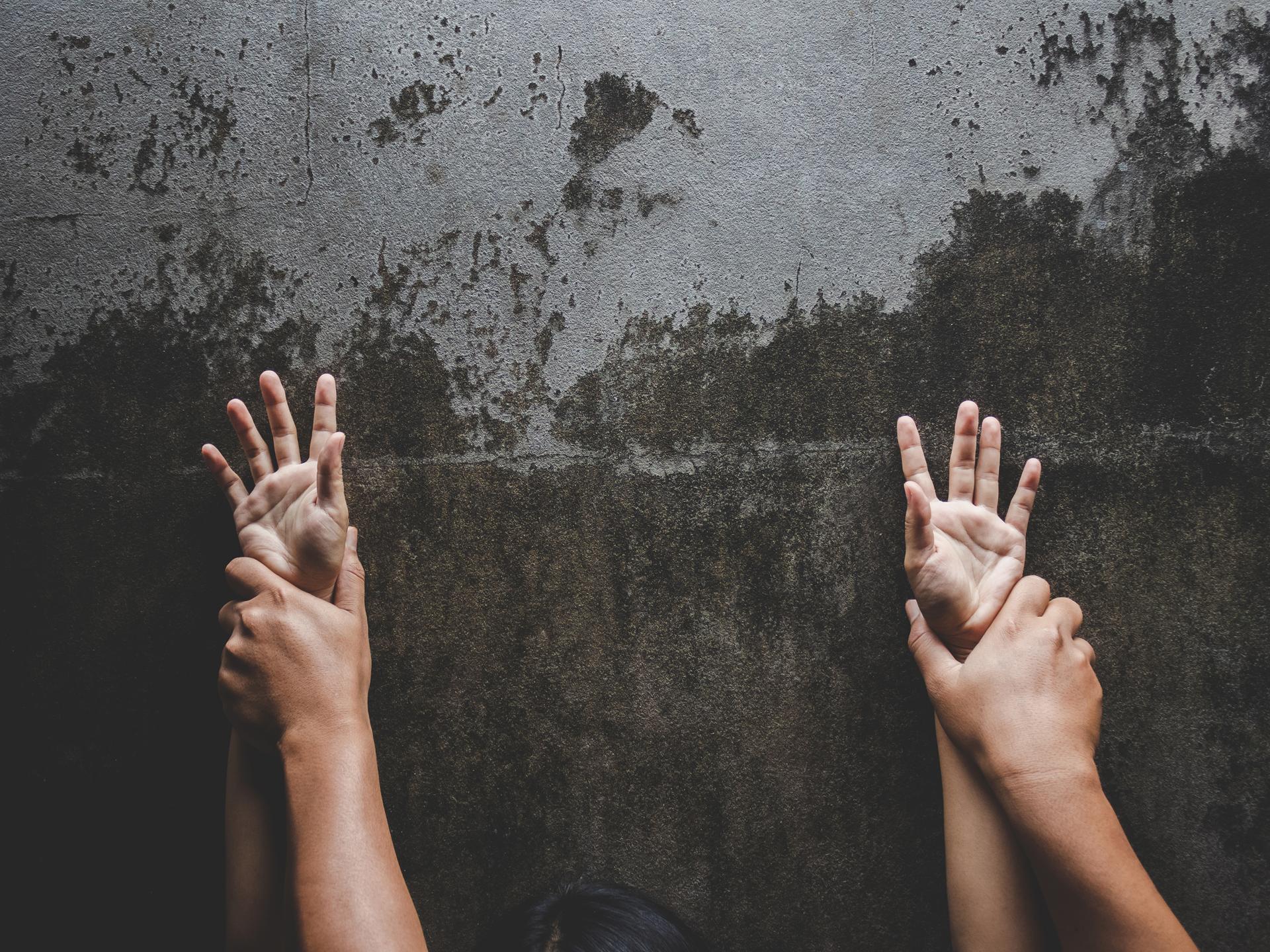 Ein paar Hände drückt ein anderes paar Hände gegen die Wand.