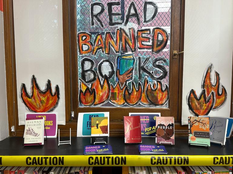 Hinter einem Büchertisch ist ein Fenster mit der denalten Aufschrift: Read banned books